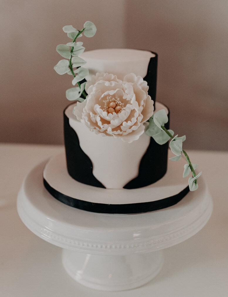 White 2 tier wedding cake wrapped in wavy edge black fondant Large white peony and eucalyptus accent between the tiers