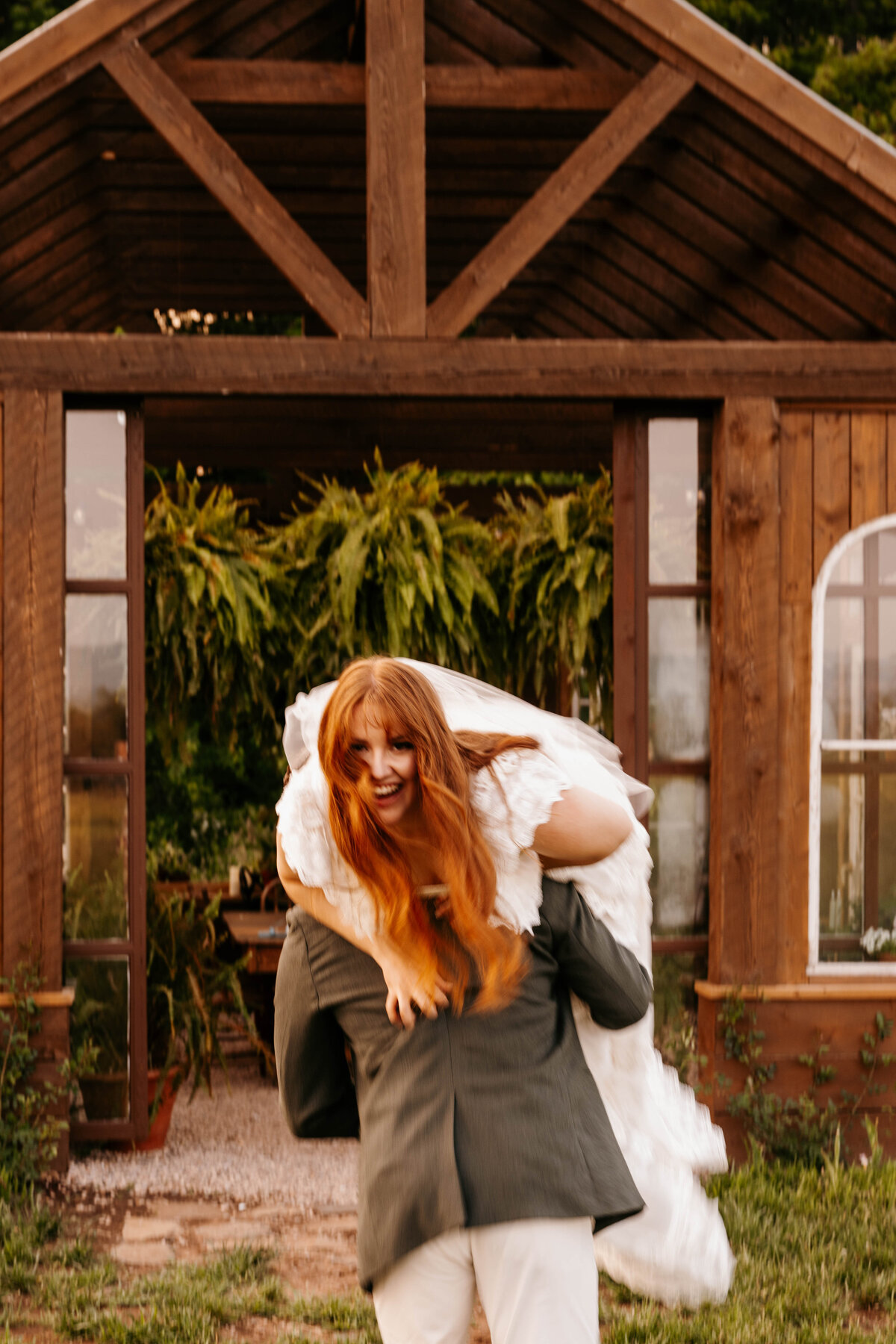 Bride, laughing as her groom carries her over his shoulder, up the stairs and across the threshold.  The Greenhouse on Strawberry Lane | Nova Scotia
