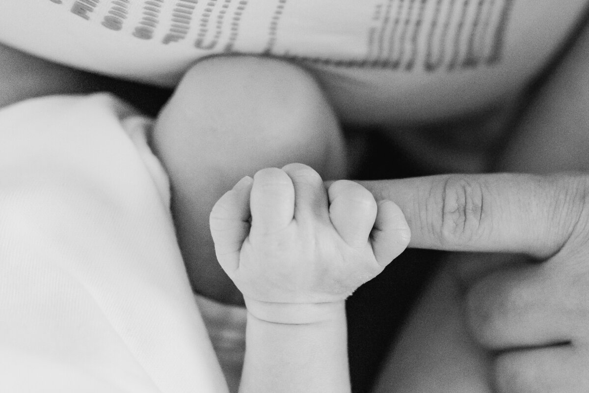 Close-up of a newborn baby's hand gently holding an adult's finger, depicted in black and white.