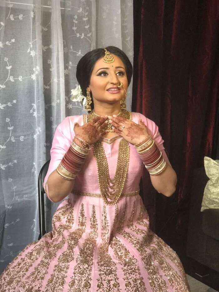 Captivating Indian bridal makeup in Ottawa, highlighted by glowing skin and a soft coral lip against her gold jewelry.