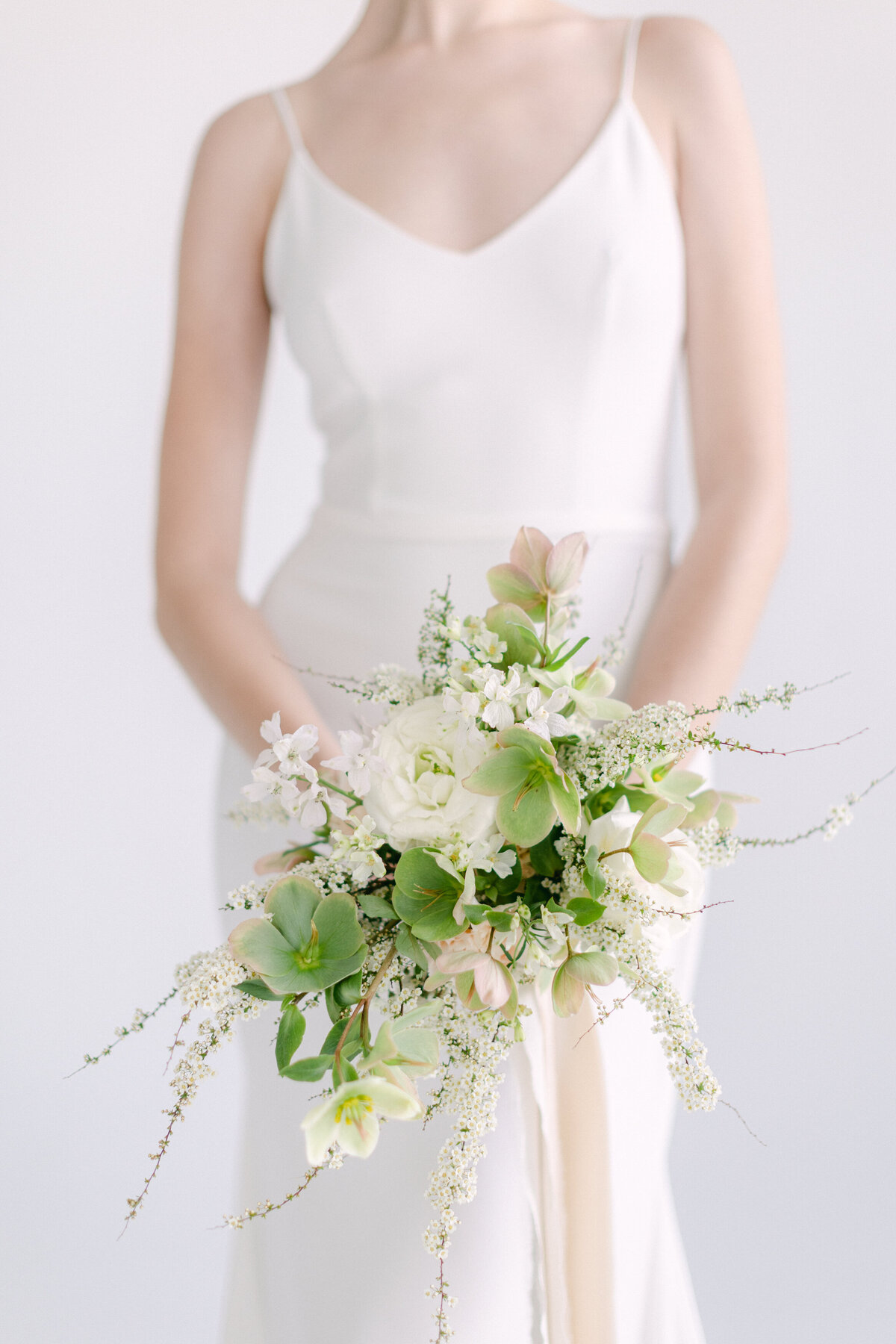 A bride holds an elegant bouquet of green and white flowers in a Montreal studio.