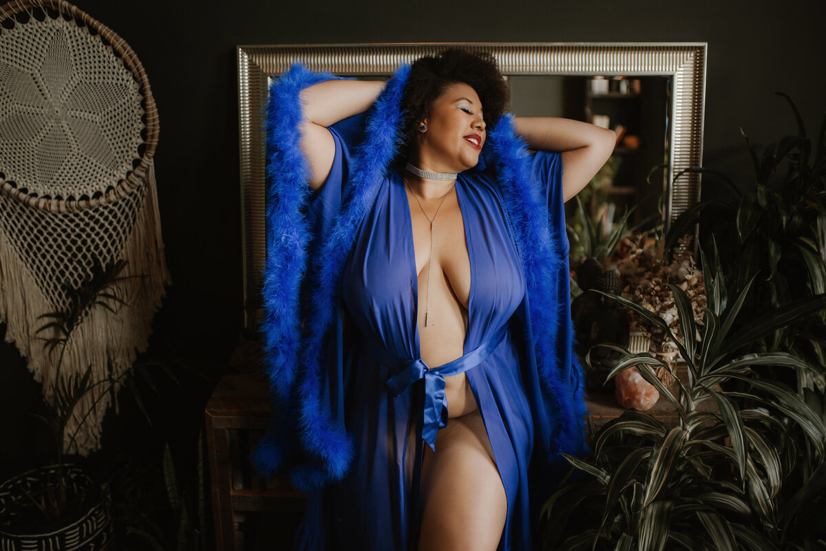 Woman wearing a blue feather robe poses in front of a mirror in the Vancouver, BC boudoir studio.