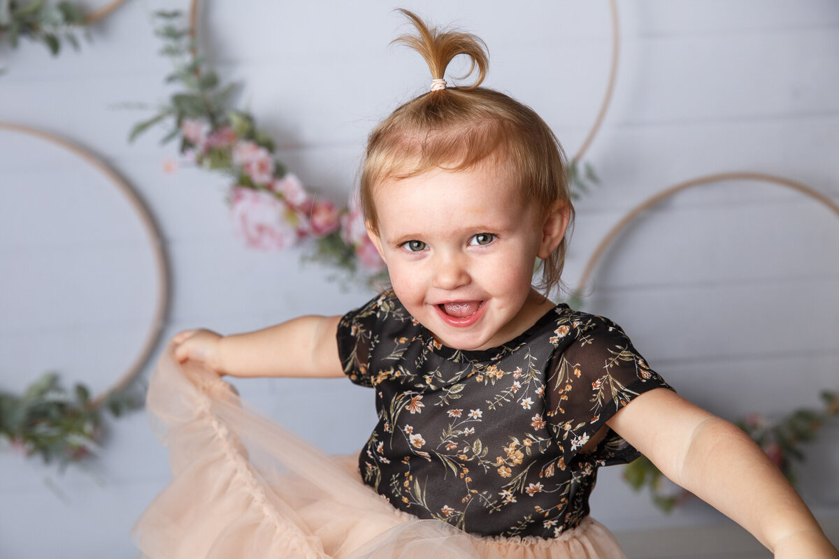 Cute toddler girl with a little pony tale on top of her head and  photographed on a floral ring background