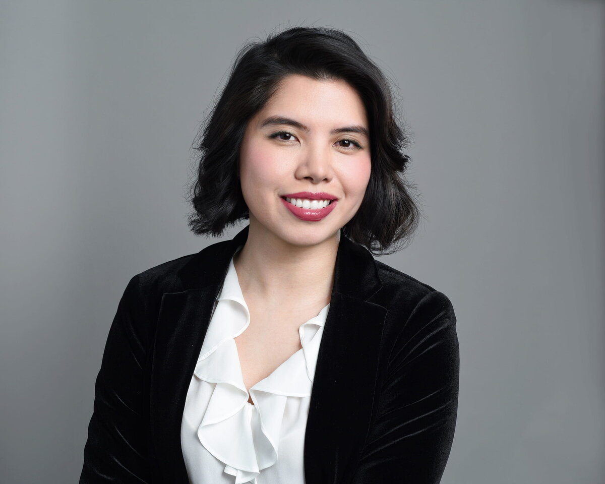 Woman in white shirt smiling with soft lighting on gray background, taken by a Toronto headshot photographer.