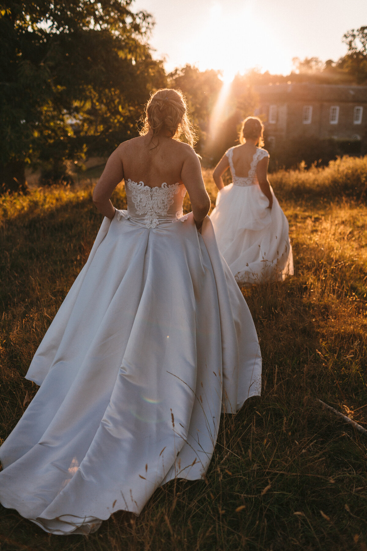 Golden Hour bridal portraits of same sex couple walking down through golden fields at Shilstone House in Devon