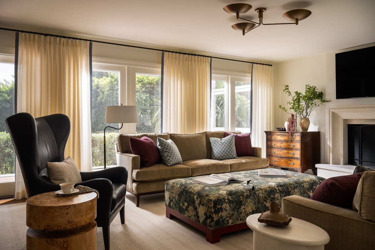Bold living room with beige couches, green velvet ottoman and patterned artwork