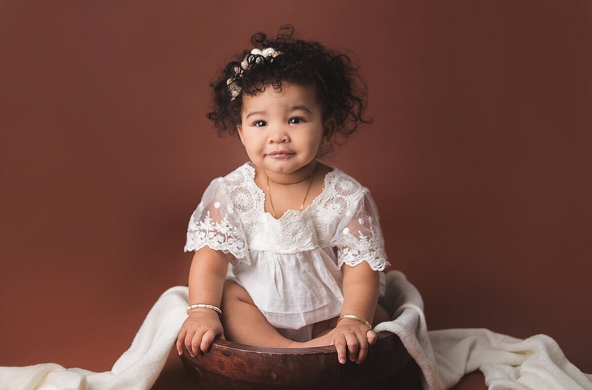 Baby girl with curly hair sitting in wood bowl during photoshoot with Nashville, TN photographer 