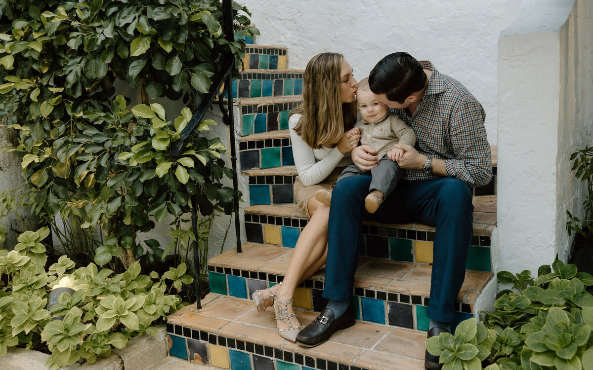 mom and dad kiss their son on stairsteps