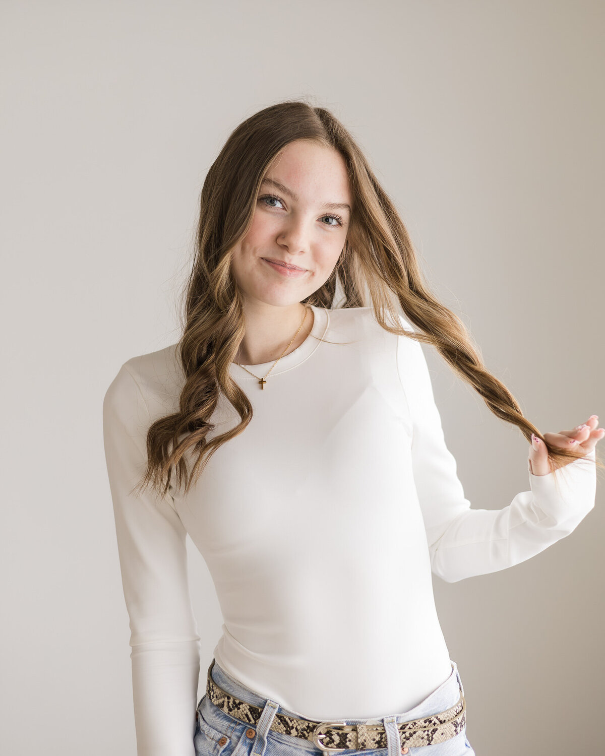 High school senior female in a studio, wearing a long sleeve white shirt, with long dark brown hair, smiling at the camera