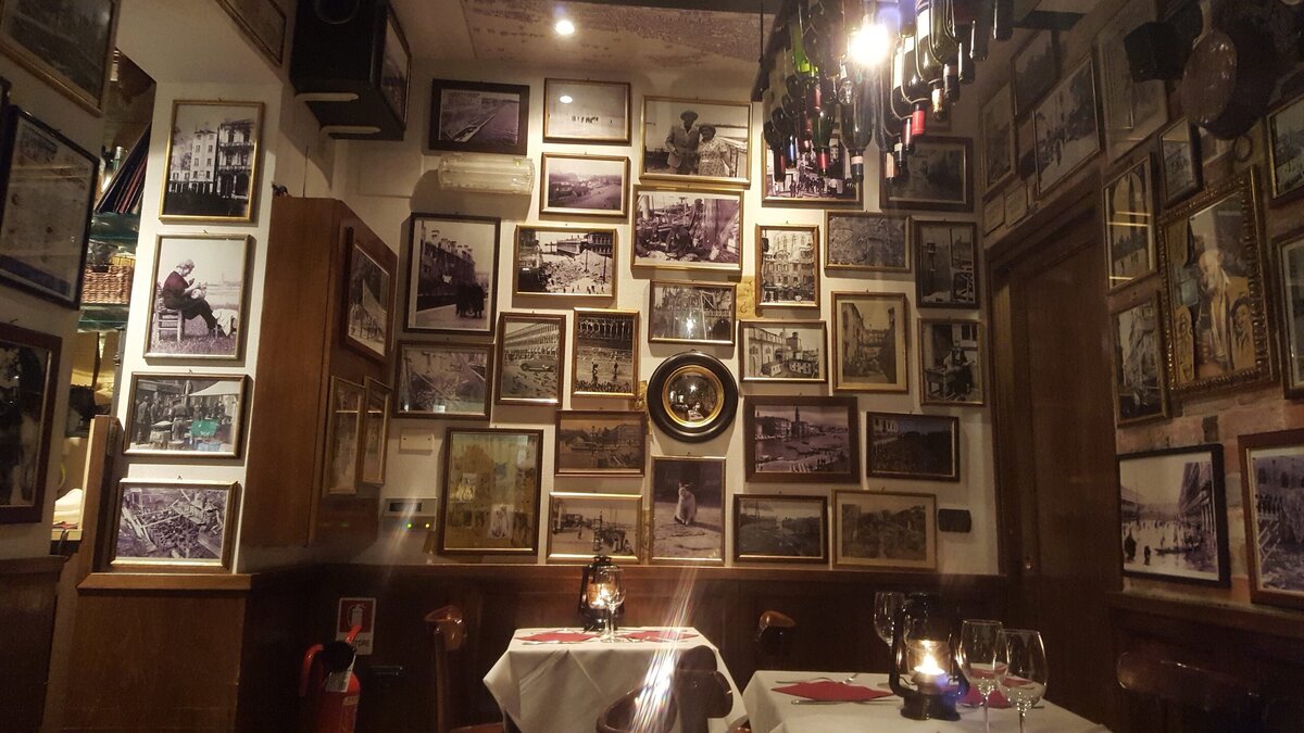 A wall featuring vintage framed photos inside the dining room of Venetian restaurant Osteria Ai Specchieri near Piazza San Marco. 