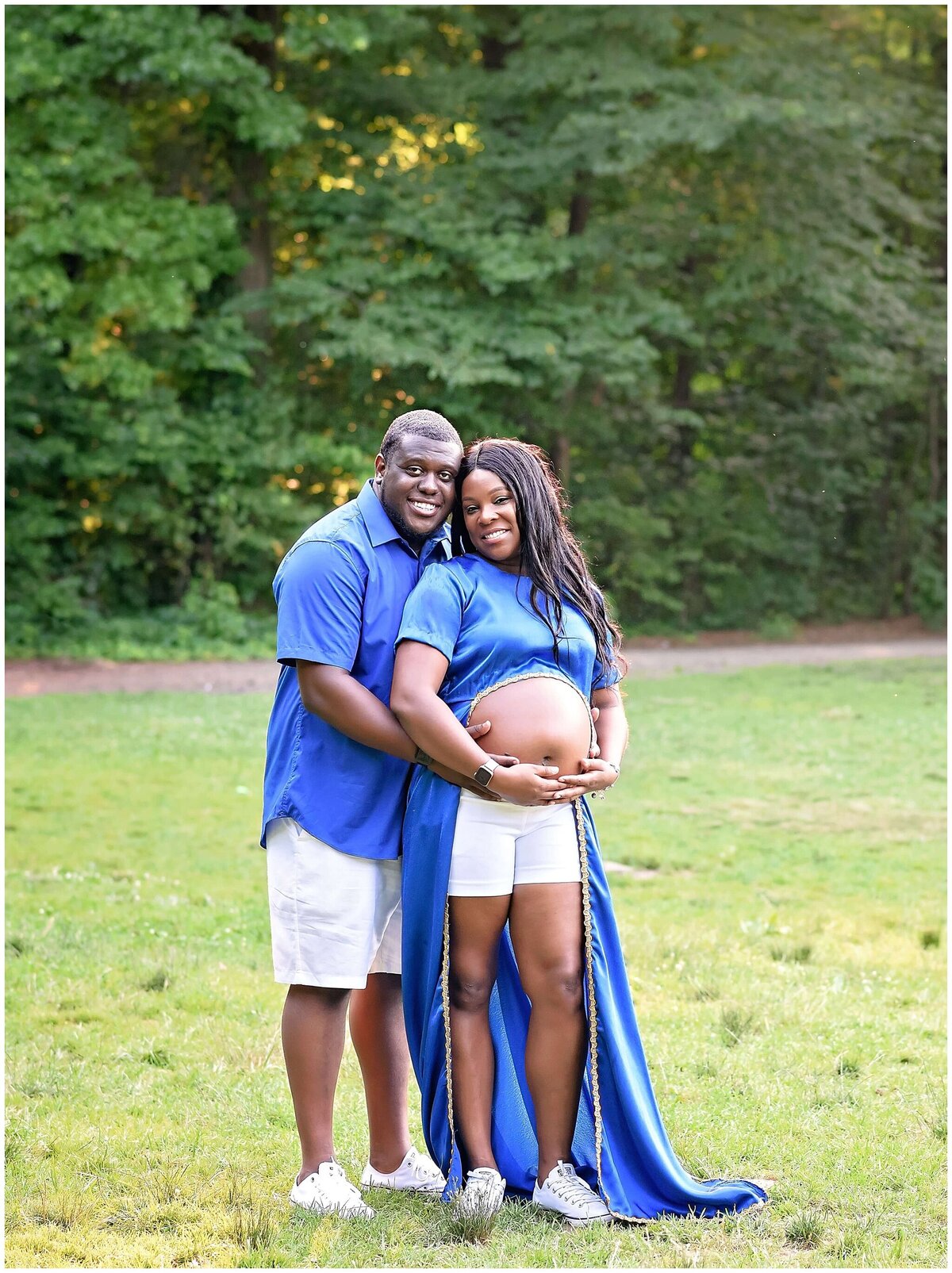 Serene outdoor setting with mother standing and father holding her belly from the back to showcase their love for their baby to be.