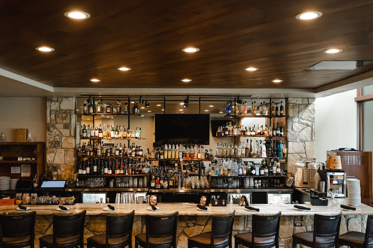 seating at restaurant bar with stone wall, wood ceiling, recessed lighting and alcohol display