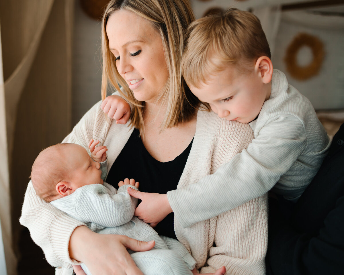 Lovely small family in Albuquerque with the mother carrying her newborn baby in a cozy outfit. The older brother looks on with affection.