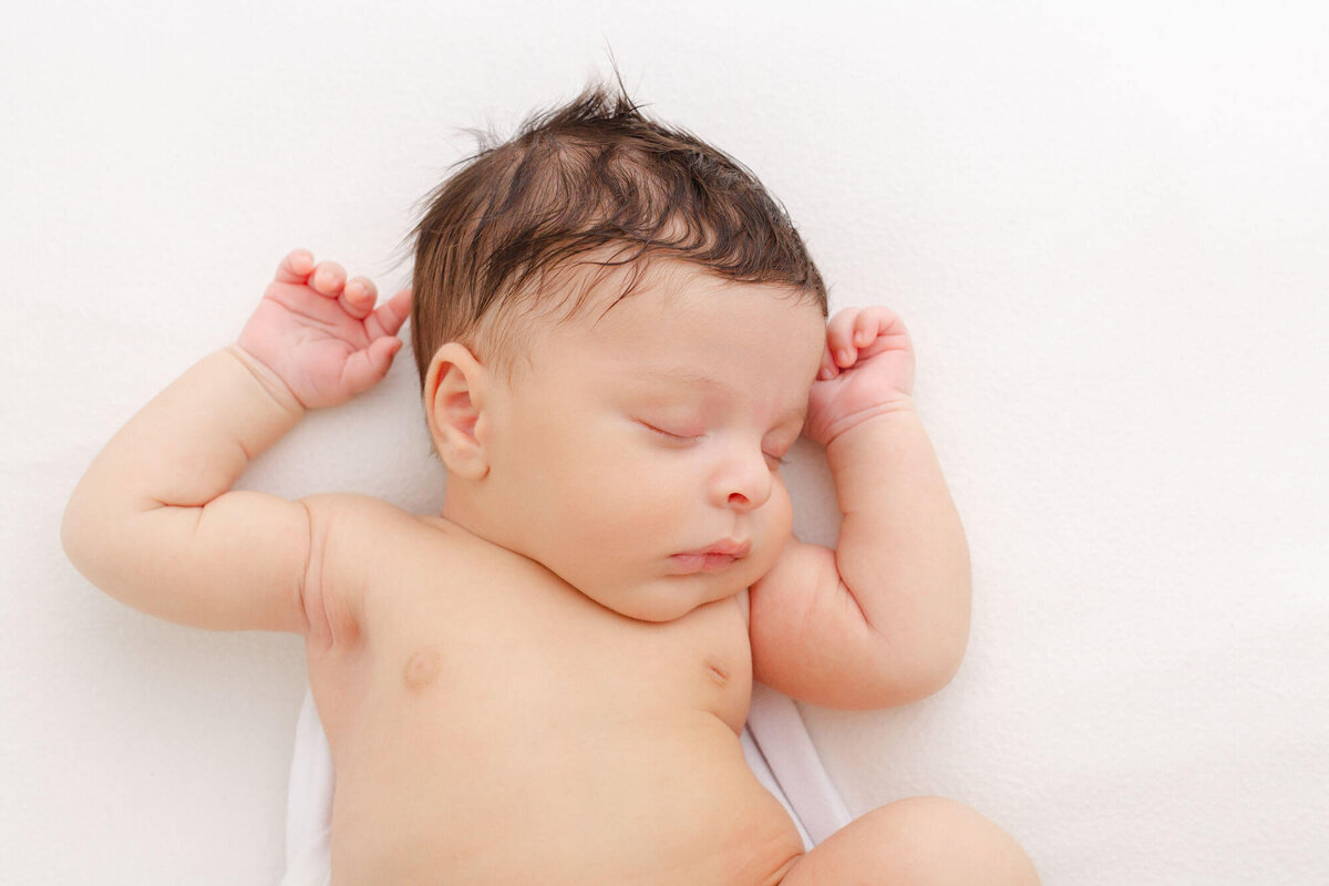 Newborn baby sleeping on a white backdrop with hands up by head  during newborn photoshoot in portland, oregon.