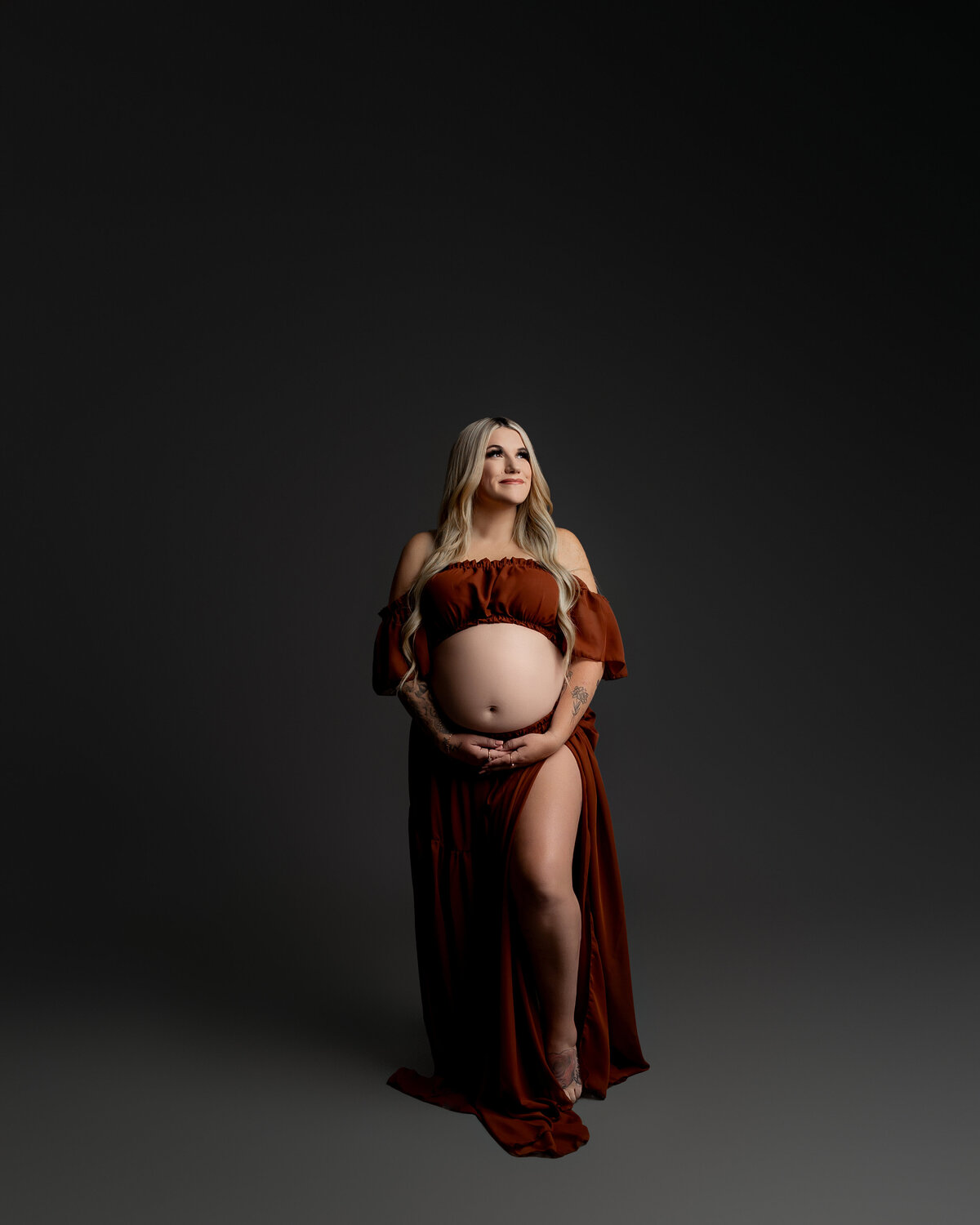 Against a dark backdrop, a mother-to-be in a striking red dress poses in profile, highlighting the beauty of her pregnancy. Captured by Inland Empire maternity photographer Kaitlyn Dawn Photography.