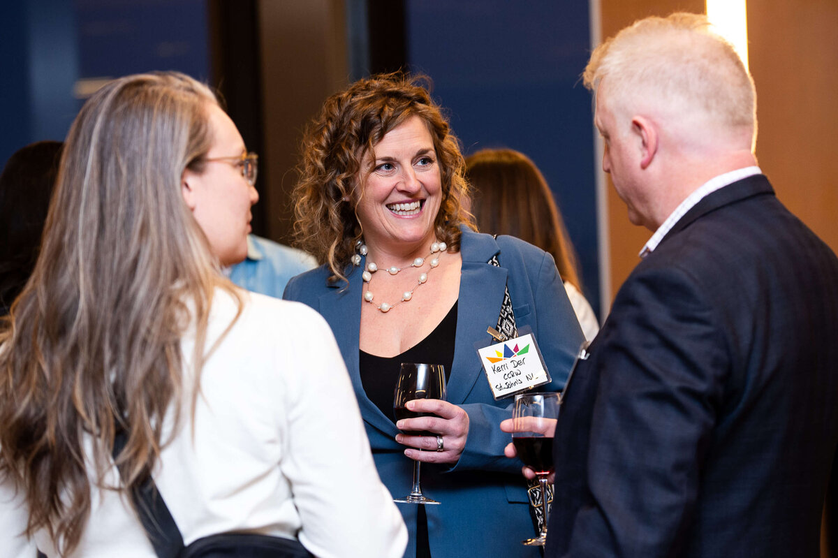 A woman with curly hair holding a glass of wine and smiling during a reception for corporate guests.  Captured by Ottawa Event Photographer JEMMAN Photography COMMERCIAL