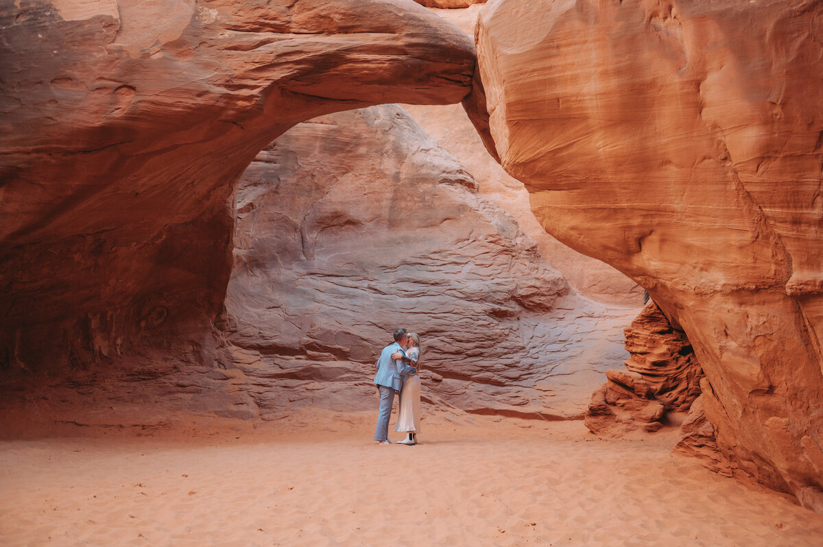 A couple kisses under a sandy arch
