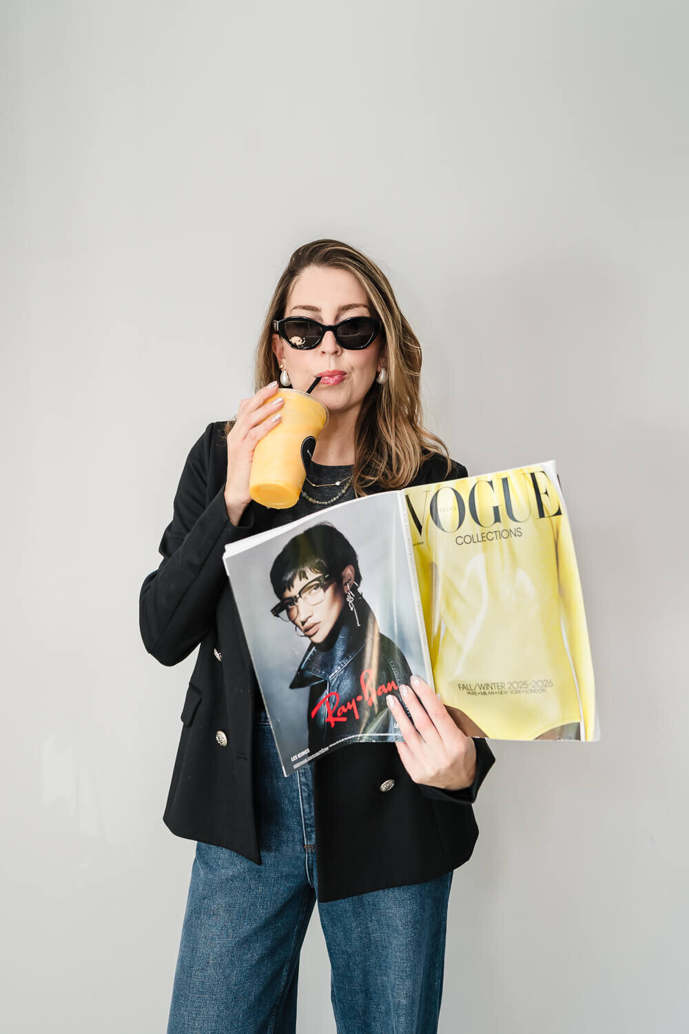 professional stylist sipping from an orange drink while reading vogue against neautral background for brand shoot