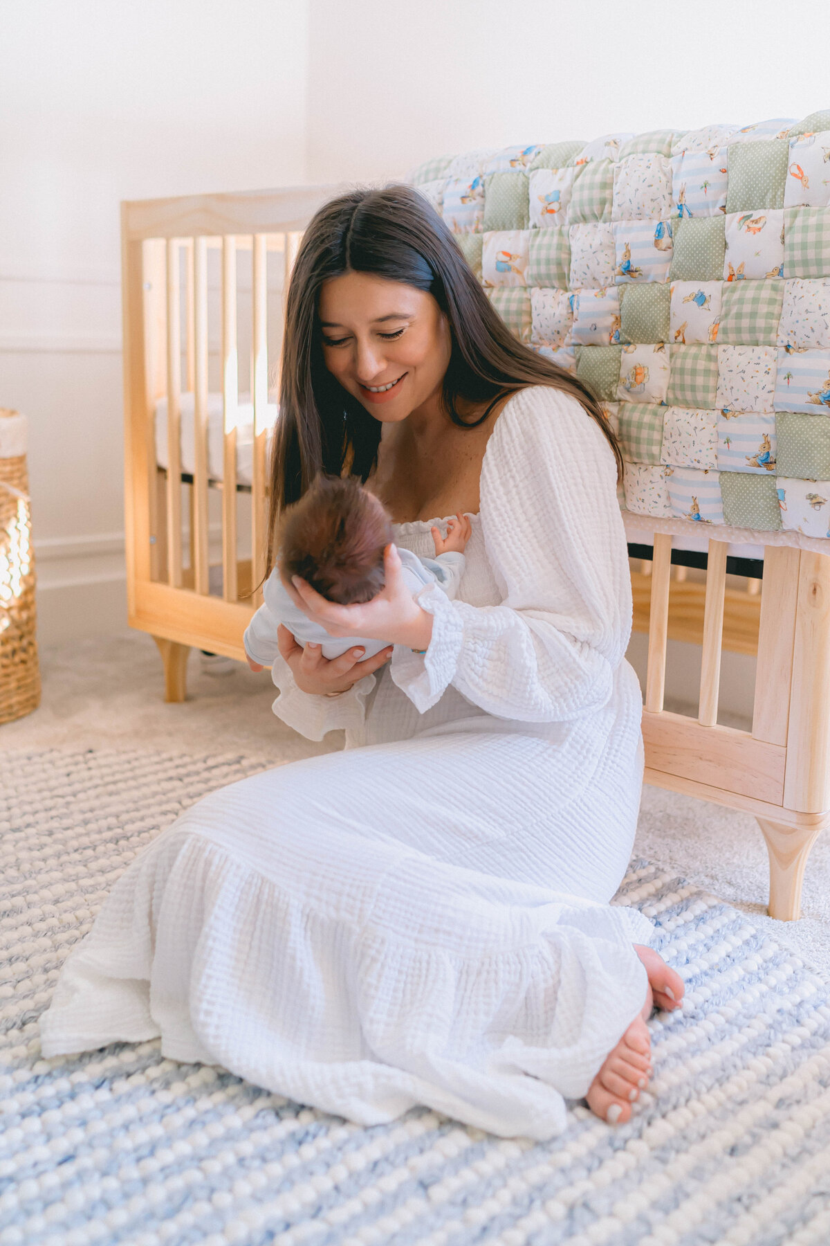 Newborn baby boy cuddled in mom’s arms near a sunlit window during an in-home newborn session in Salt Lake City, captured by a Salt Lake City newborn photographer.