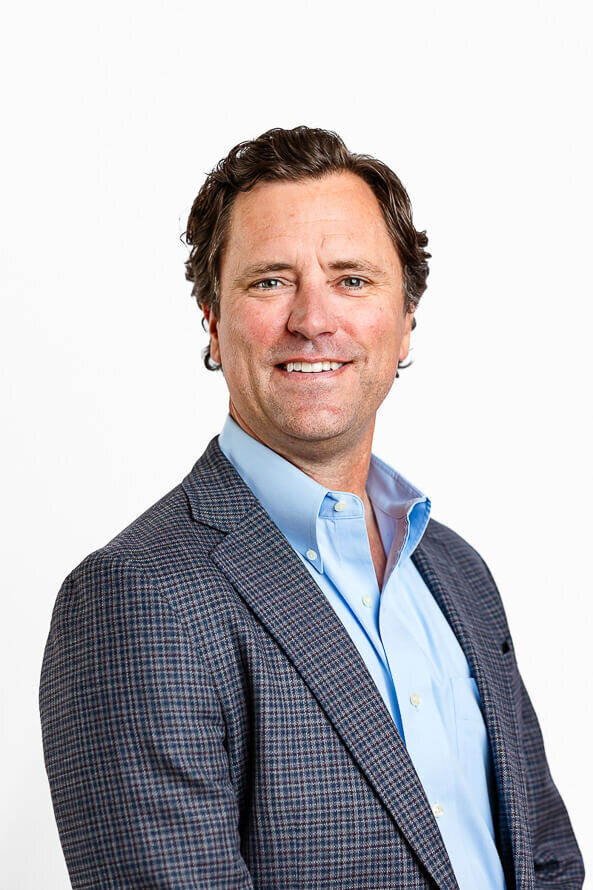 Man turns sideways and smiles in a white studio.