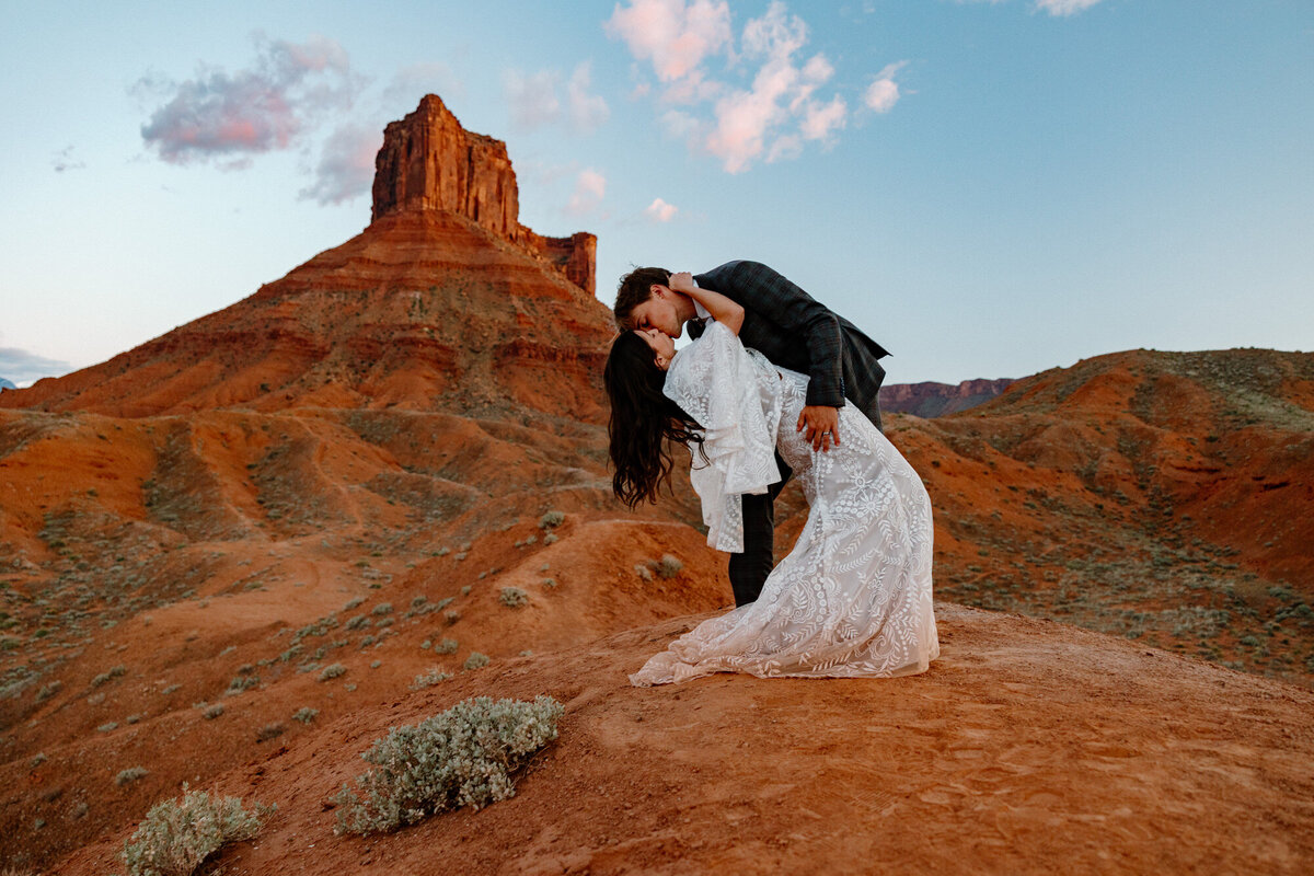 A bride and groom share their first kiss during their wedding ceremony in Moab. They are surrounded by epic red rock structures. 