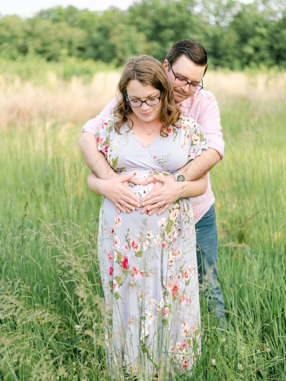 Mom in floral dress with dad wrapping his arms around pregnant belly.