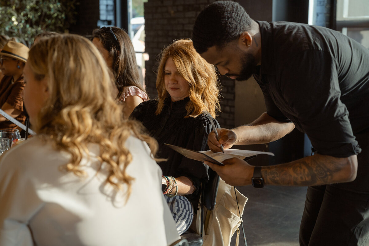 A candid moment of a guest placing her dinner order at STIRR in Dallas. The image captures the relaxed, elegant atmosphere of the private networking event, showcasing the personalized experience of the evening.