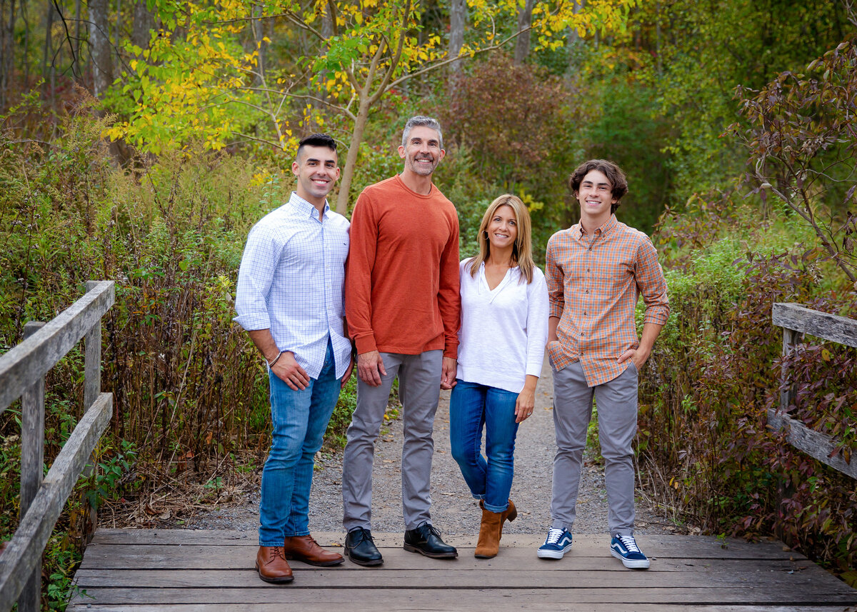 Family portrait taken of a high school senior guy from Victor, NY with his family on a bridge in the fall