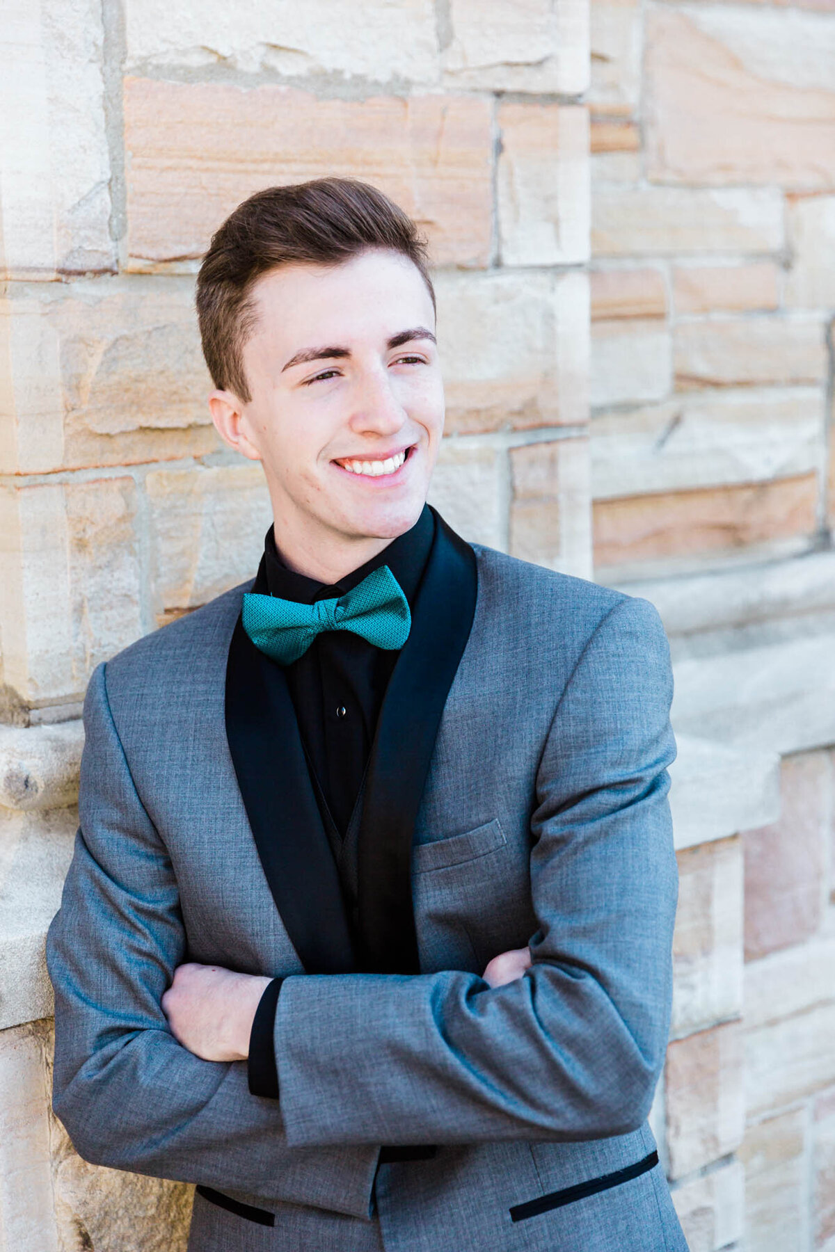 Portrait of a guy in a tuxedo for his senior prom leaning against a brick wall.