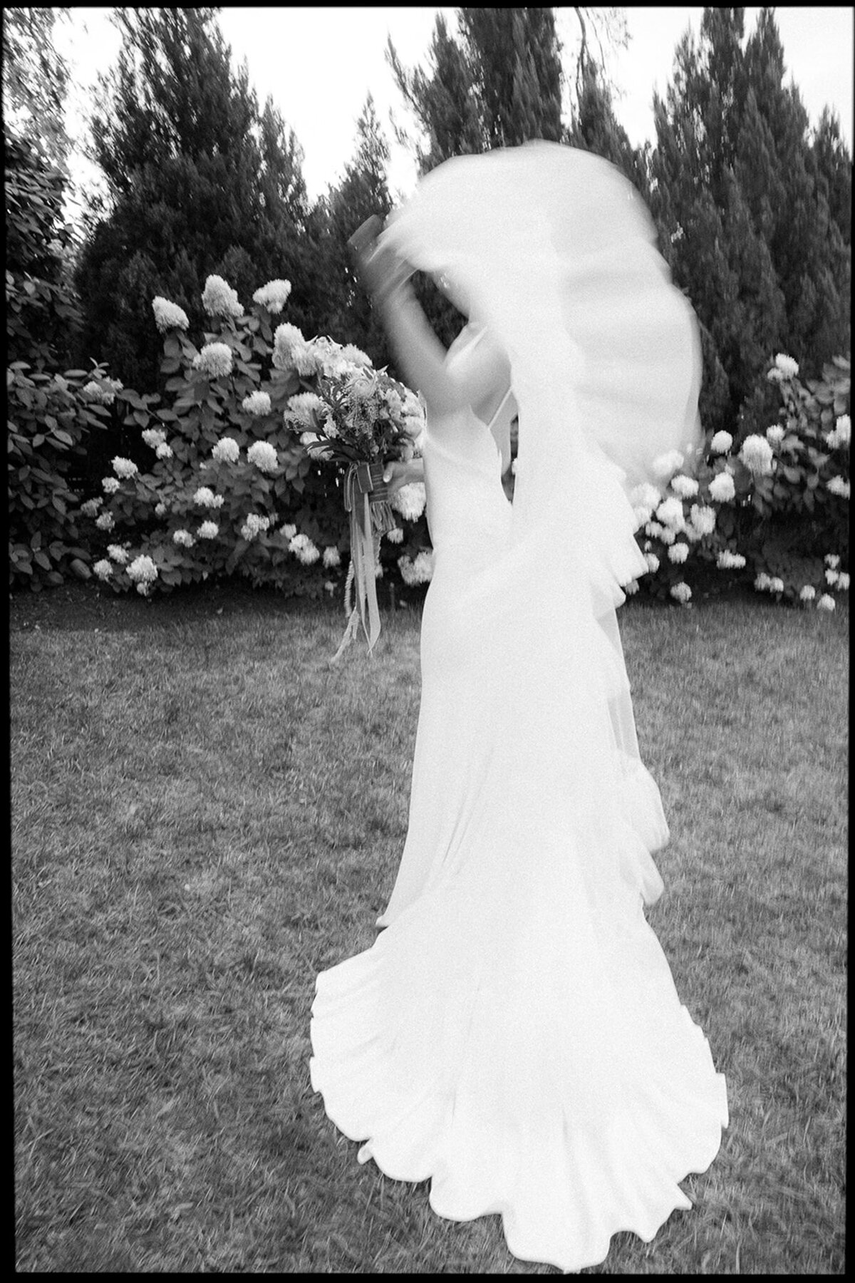 Candid of a bride photographed in black and white dramatically tossing her veil.