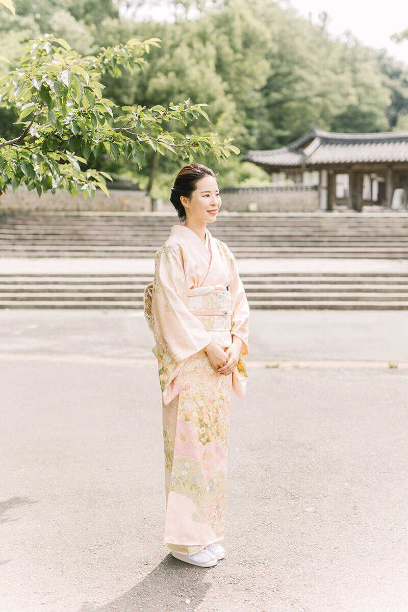 A woman wearing a pink orange kimono, standing in front of  a sakura tree in early summer. Shot by Yukika Ishikawa Photography at Yokohama, Tokyo .