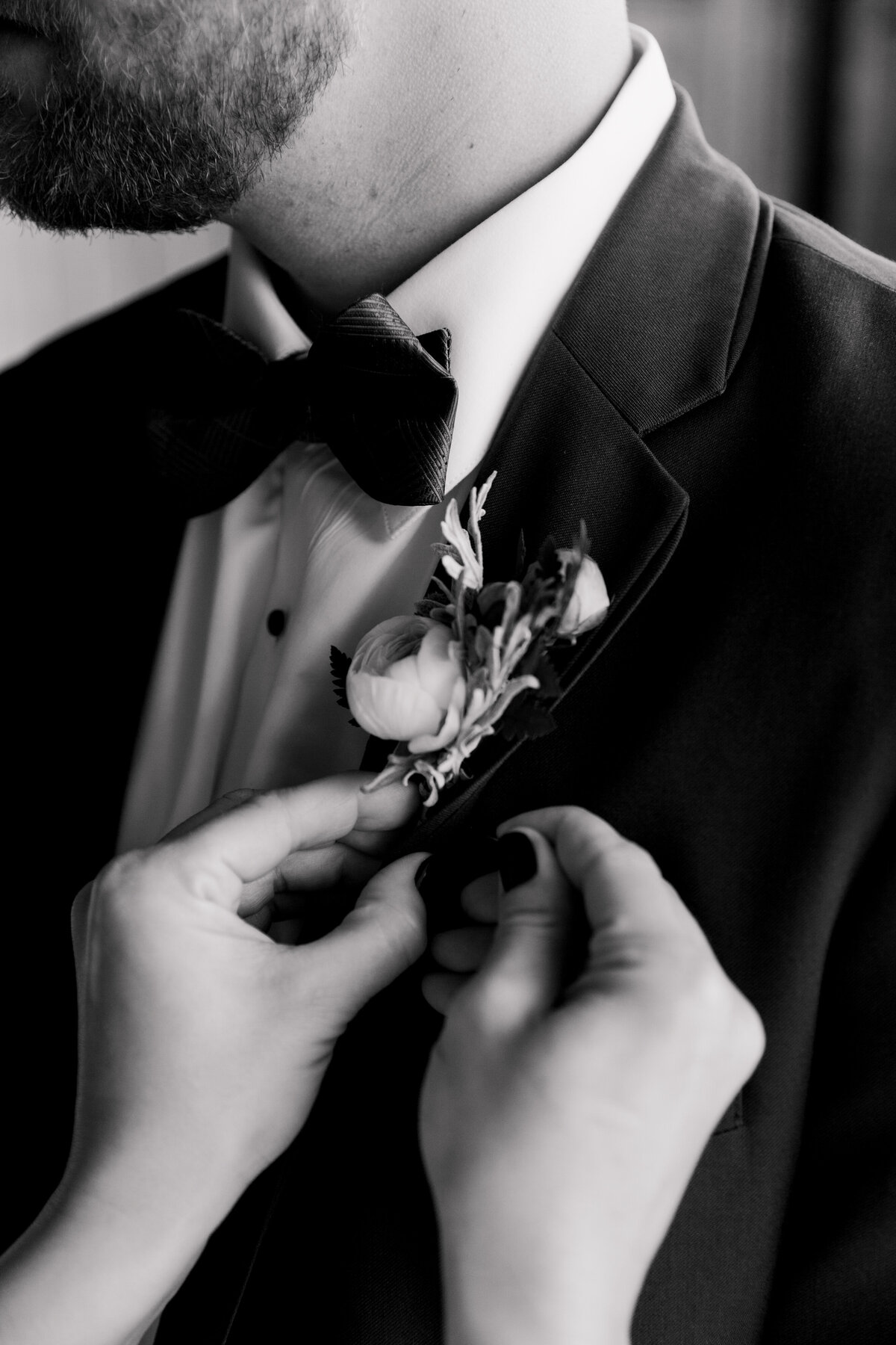 Black and white close-up of hands pinning on groom's boutonniere