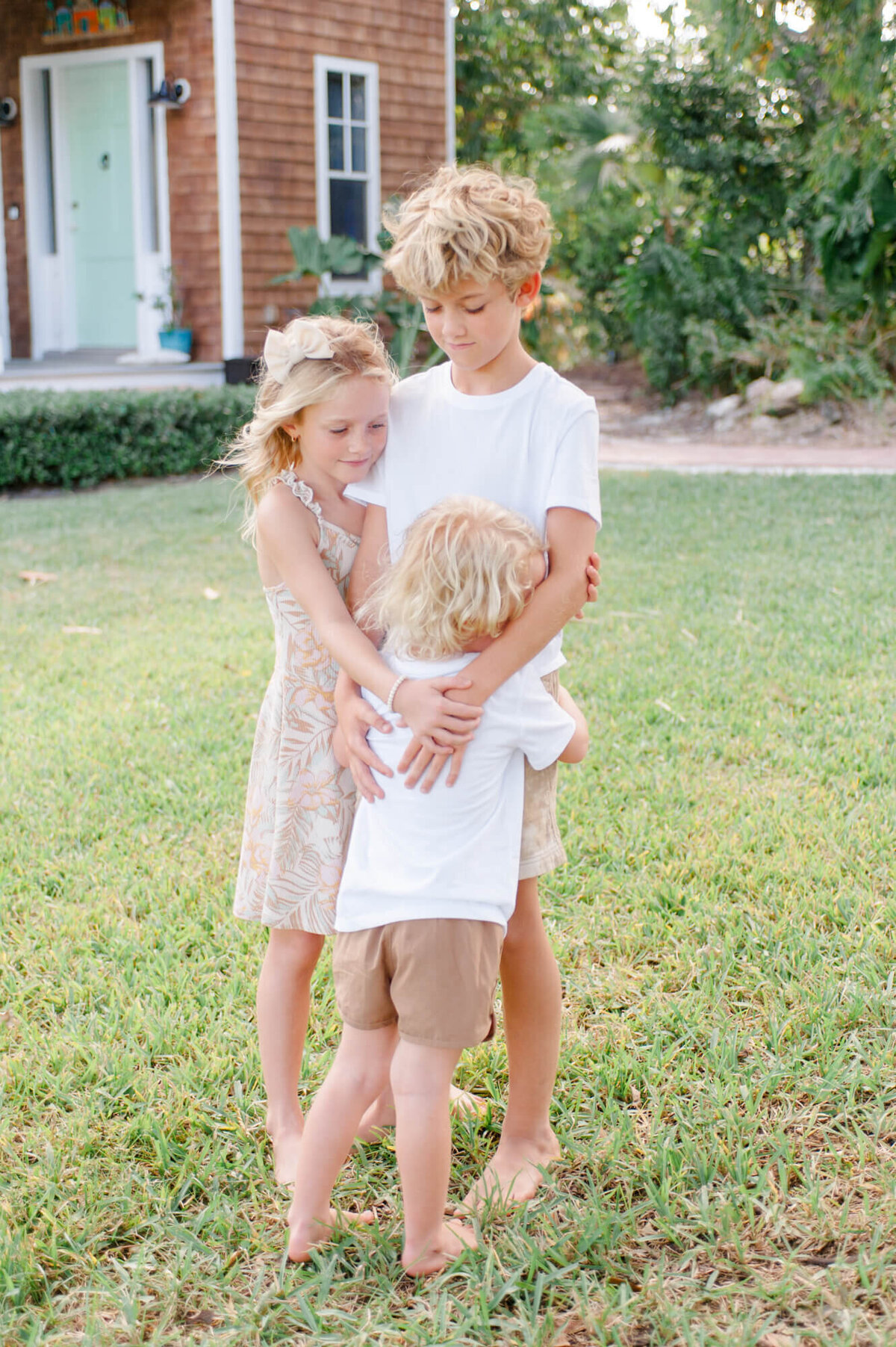 Three siblings stand in the yard hugging during their family photography photoshoot