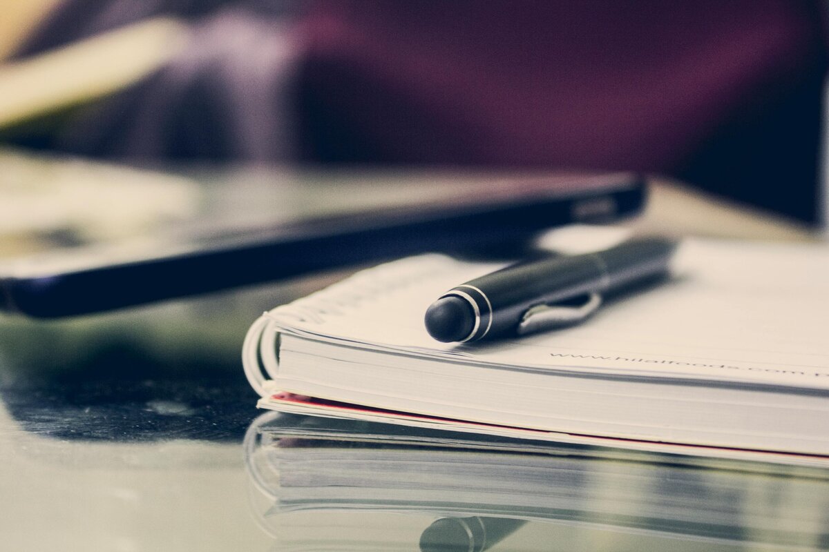 A zoomed in view of an Apple laptop with an open notebook  and cup of coffee beside of it