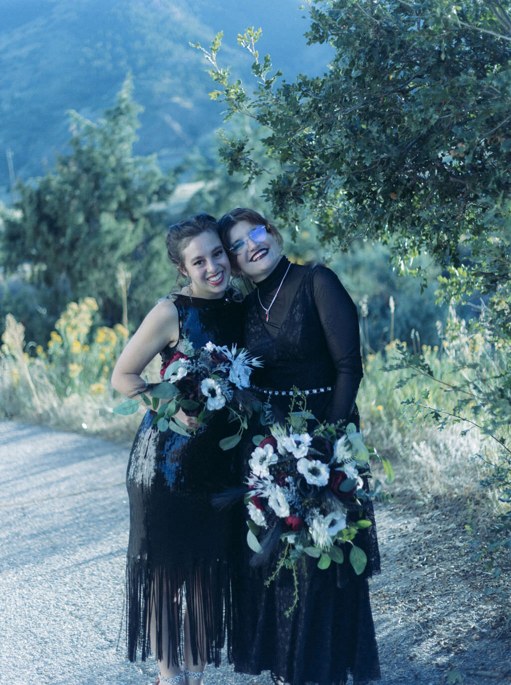 Two people in black dresses smiling together.