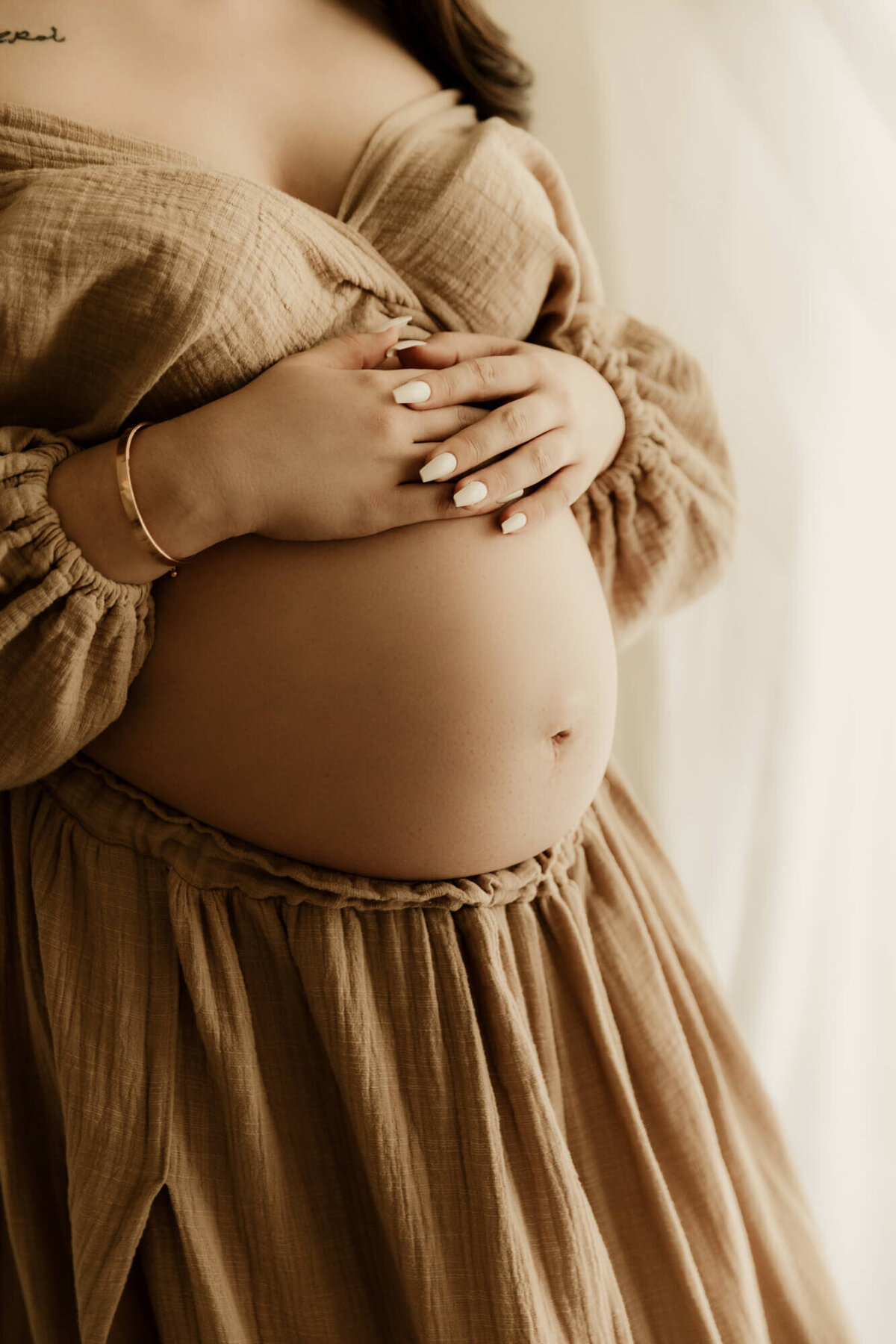 Baby bump portrait of a mother wearing a beige skirt and top.