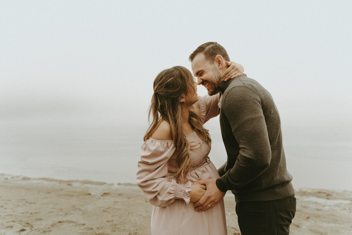 photo of a pregnant wife and husband about to kiss at a foggy beach
