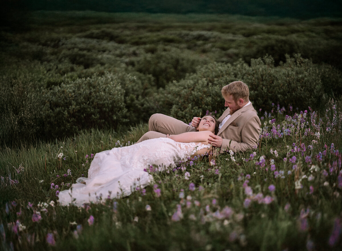 Bride and groom lay together in a field of flowers during Banff elopement