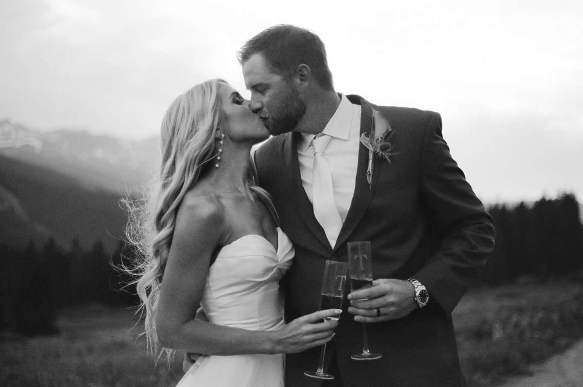 bride and groom kissing while holding champagne glasses