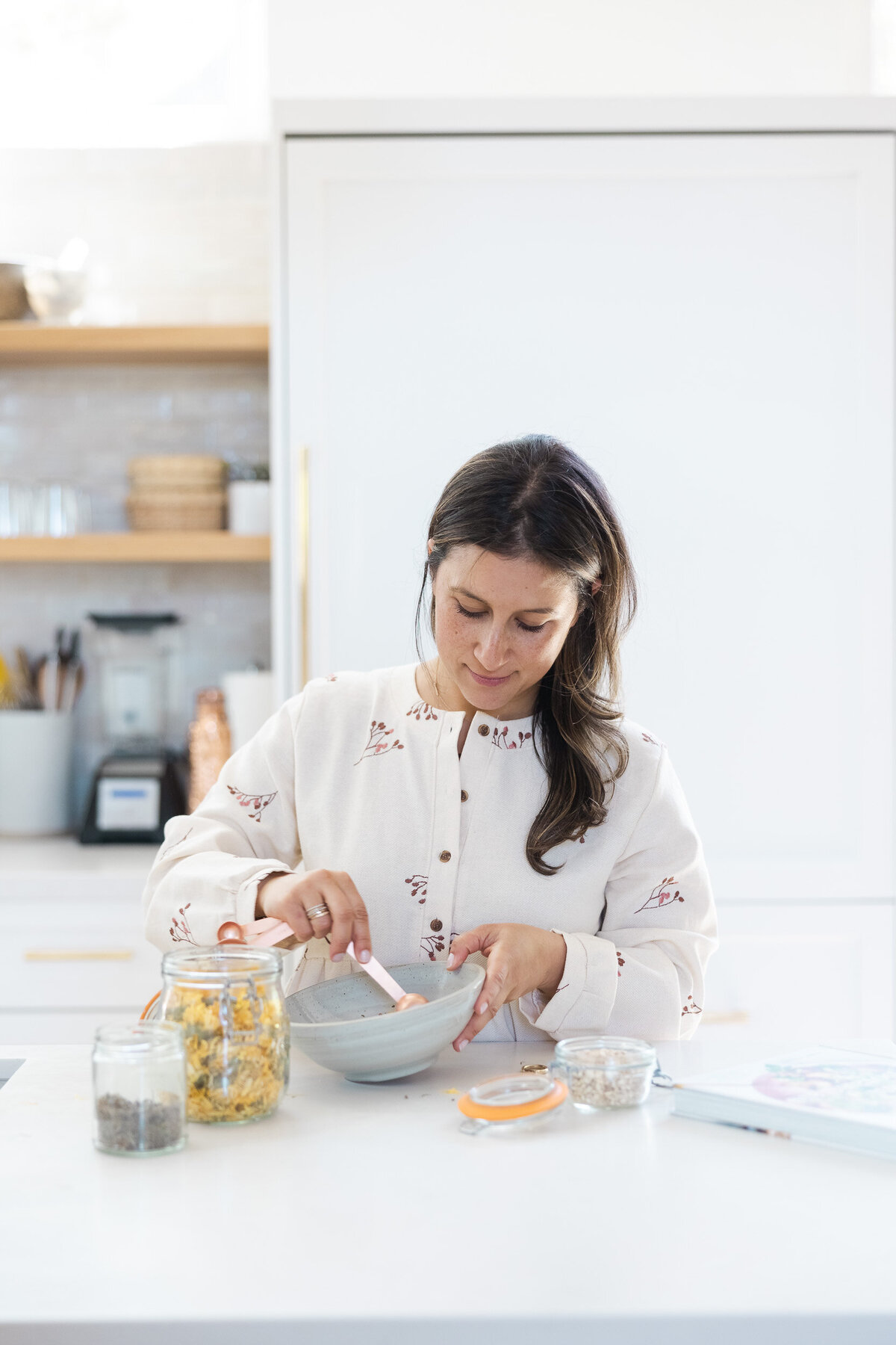 Woman in a neutral bright kitchen  working with her ayurvedic herbs.