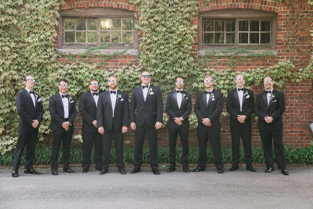 Groomsmen stand in front of ivy covered wall at The Hermitage Museum