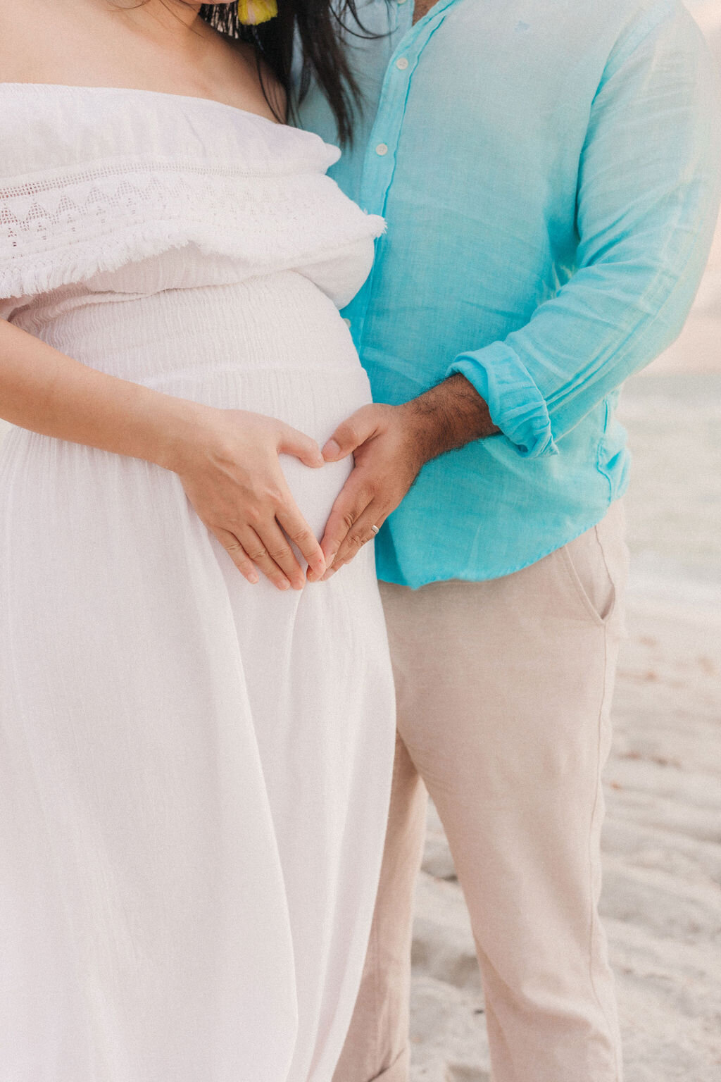 Expecting couple creating a heart shape with their hands over the baby bump during a maternity session on the beach in Palm Beach, South Florida.