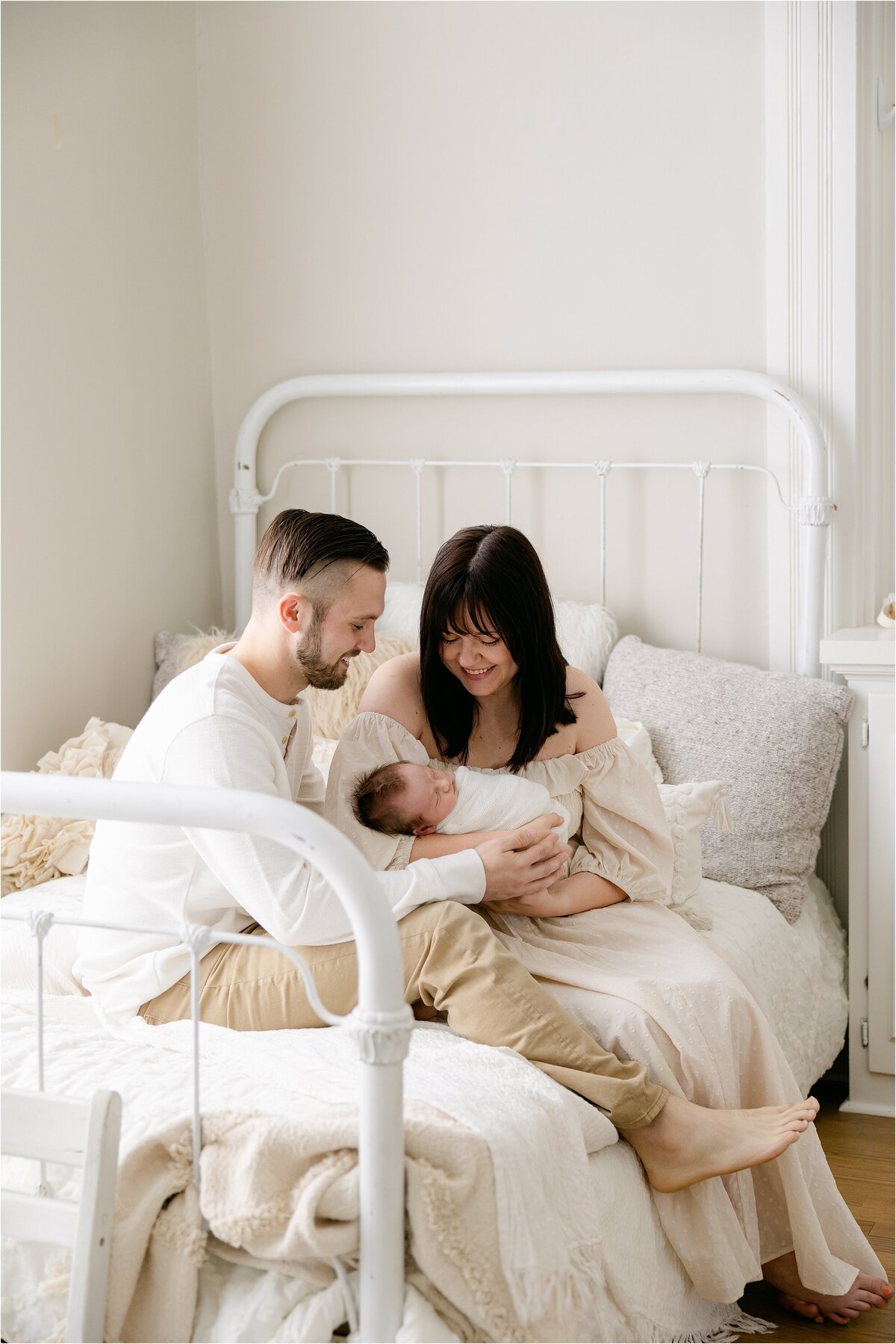 couple sitting on white bed looking at their newborn baby boy