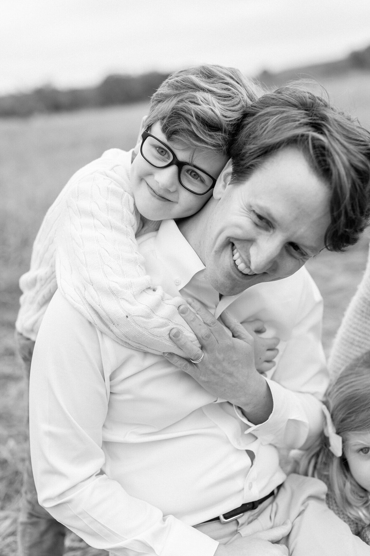 Black and white image of a son hugging his dad from behind, taken during a family photography session with Abby Park Photography