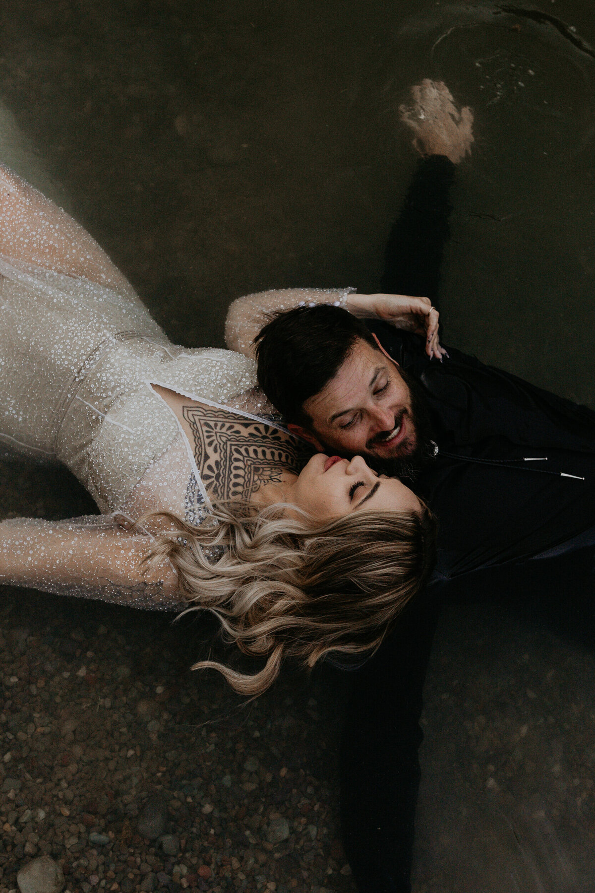 bride and groom laying together in a pond in their wedding attire