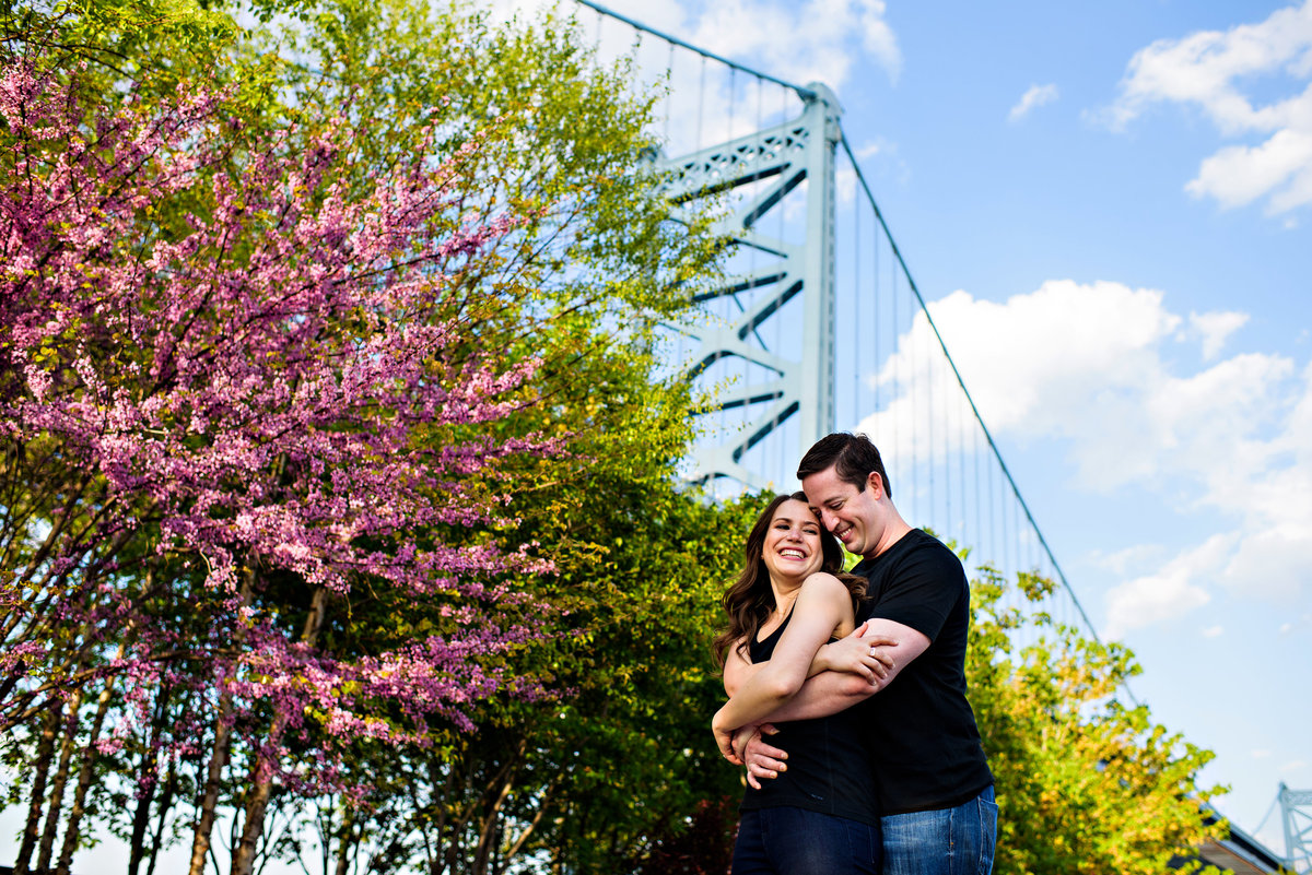 A man holds his girlfriend with the philly bridge in the background.