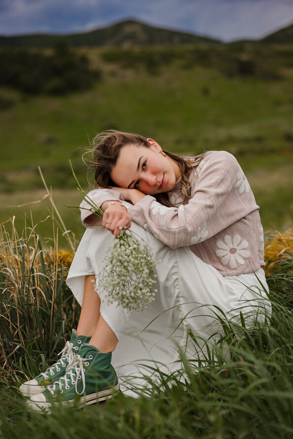 Girl with somber look puts head on knees in a grassy field.