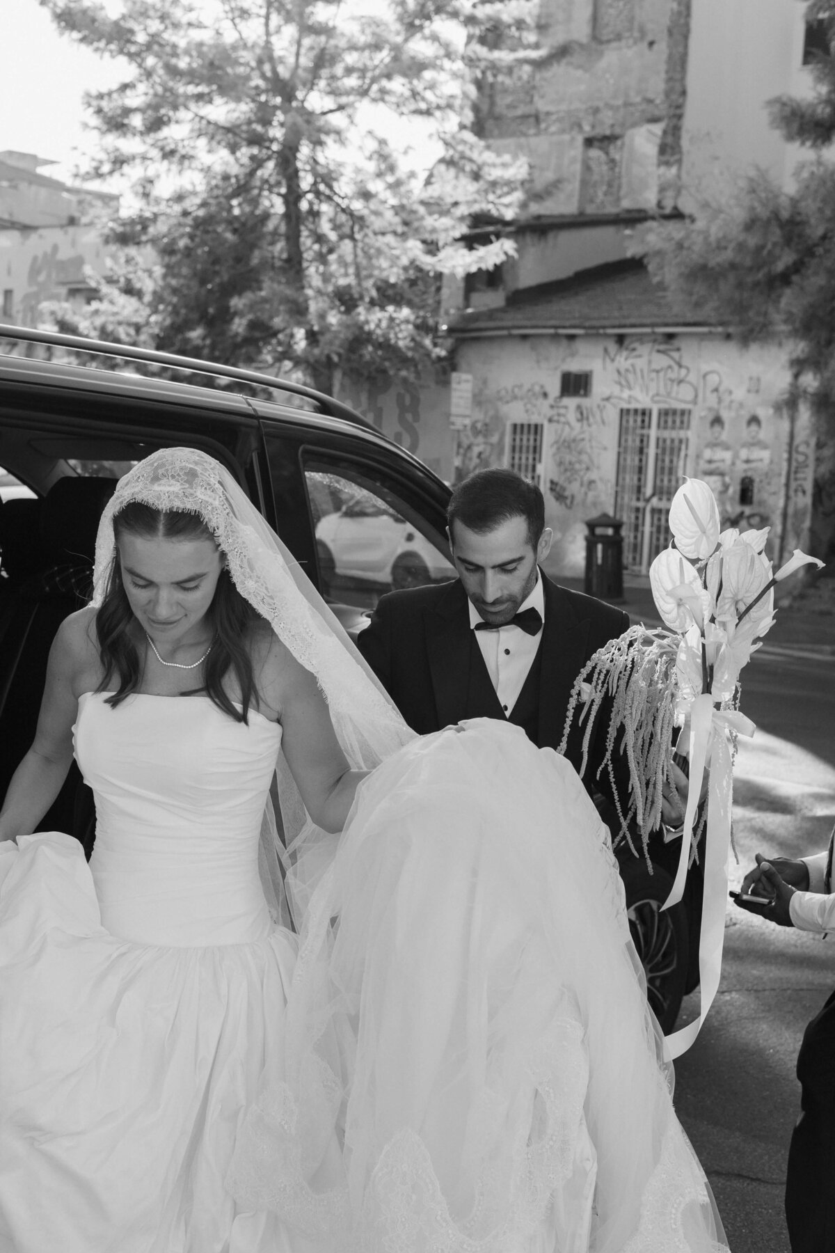 Bride stepping out of car with groom’s assistance before entering venue

