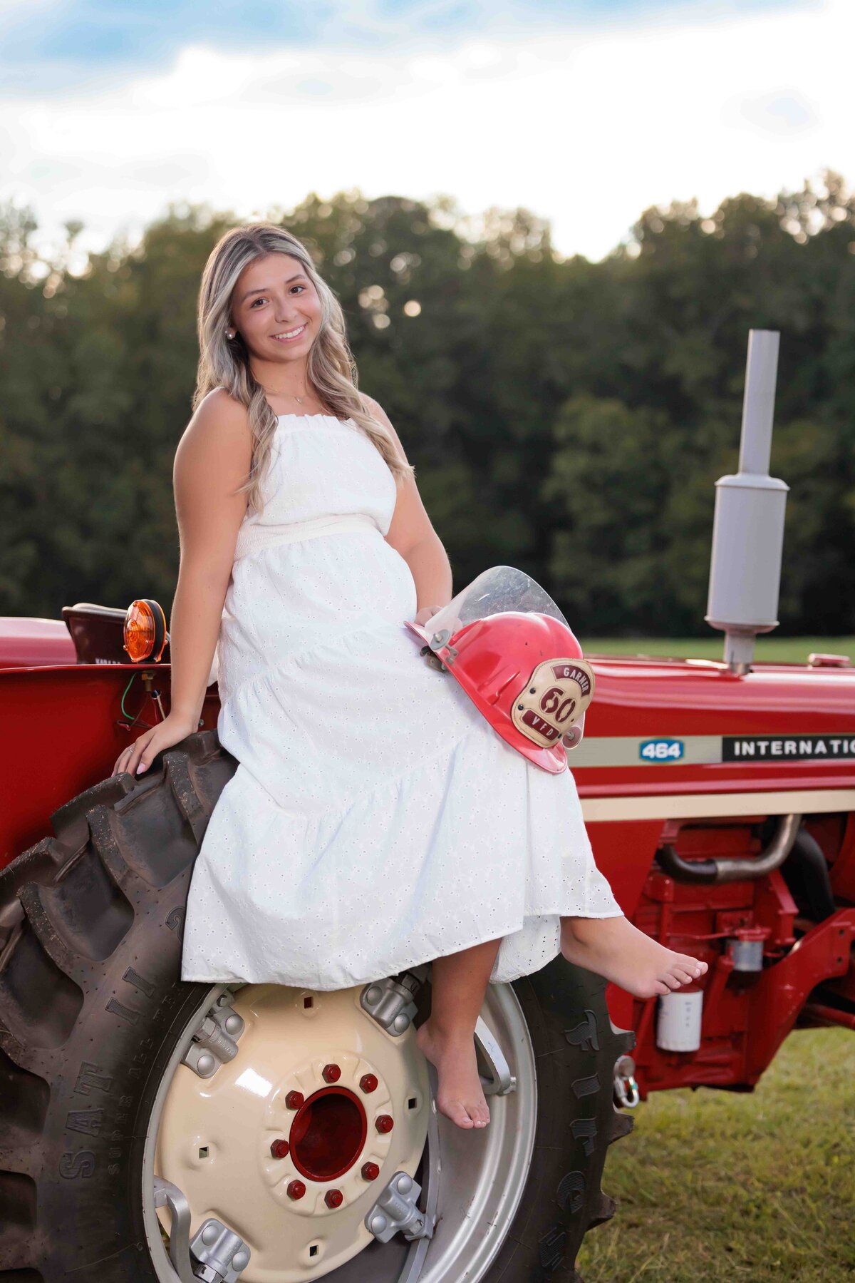 High School Senior sitting on her grandfathers tractor holding his fireman's helmet for sweet senior pictures.