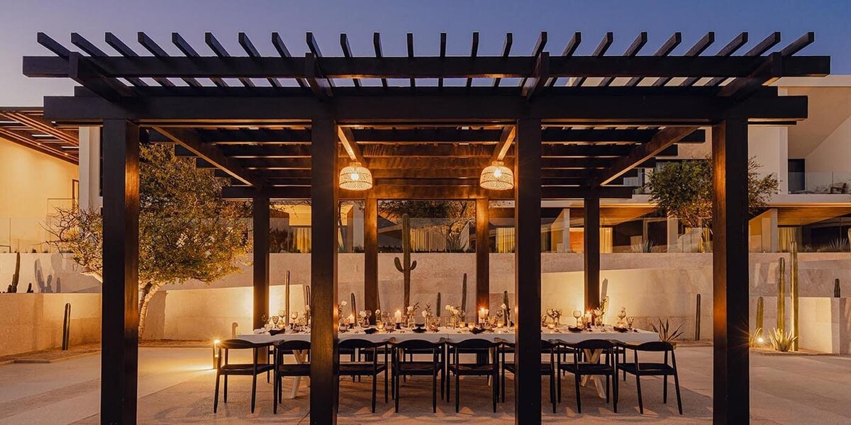 An elegant outdoor dining setup at Nobu Los Cabos, featuring a candlelit table under a modern pergola with warm lighting and desert landscaping. 